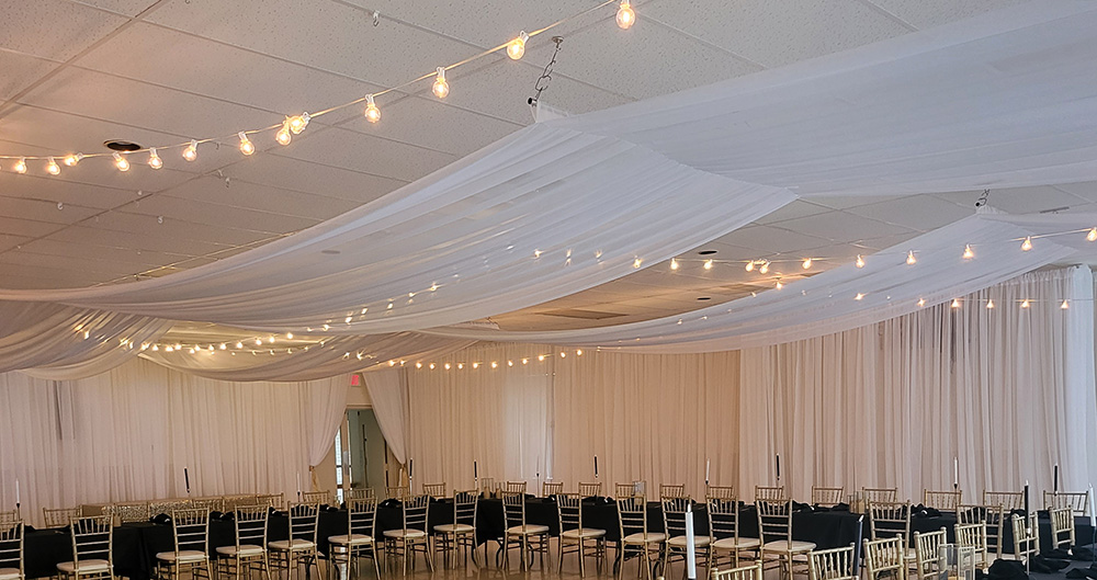 White linear ceiling draping with bistro lights and wall draping. 