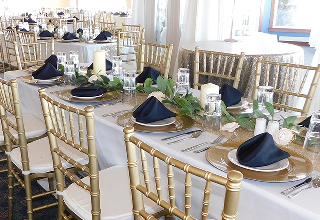 Navy napkins on gold chargers with flatware and glasses at each seat. 