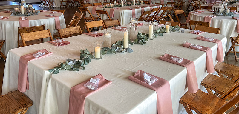 Ivory table linens with rose colored napkins and party favors at each seat. 