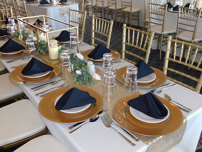Navy napkins on gold chargers with flatware and glasses at each seat. 