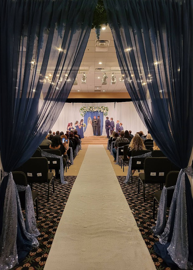 Ceremony with draping, floral accents, and white aisle runner. 