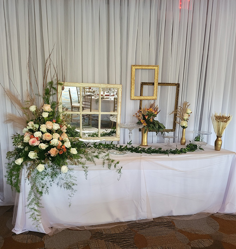 Huge flower arrangement on dessert table with frames hanging behind the table.