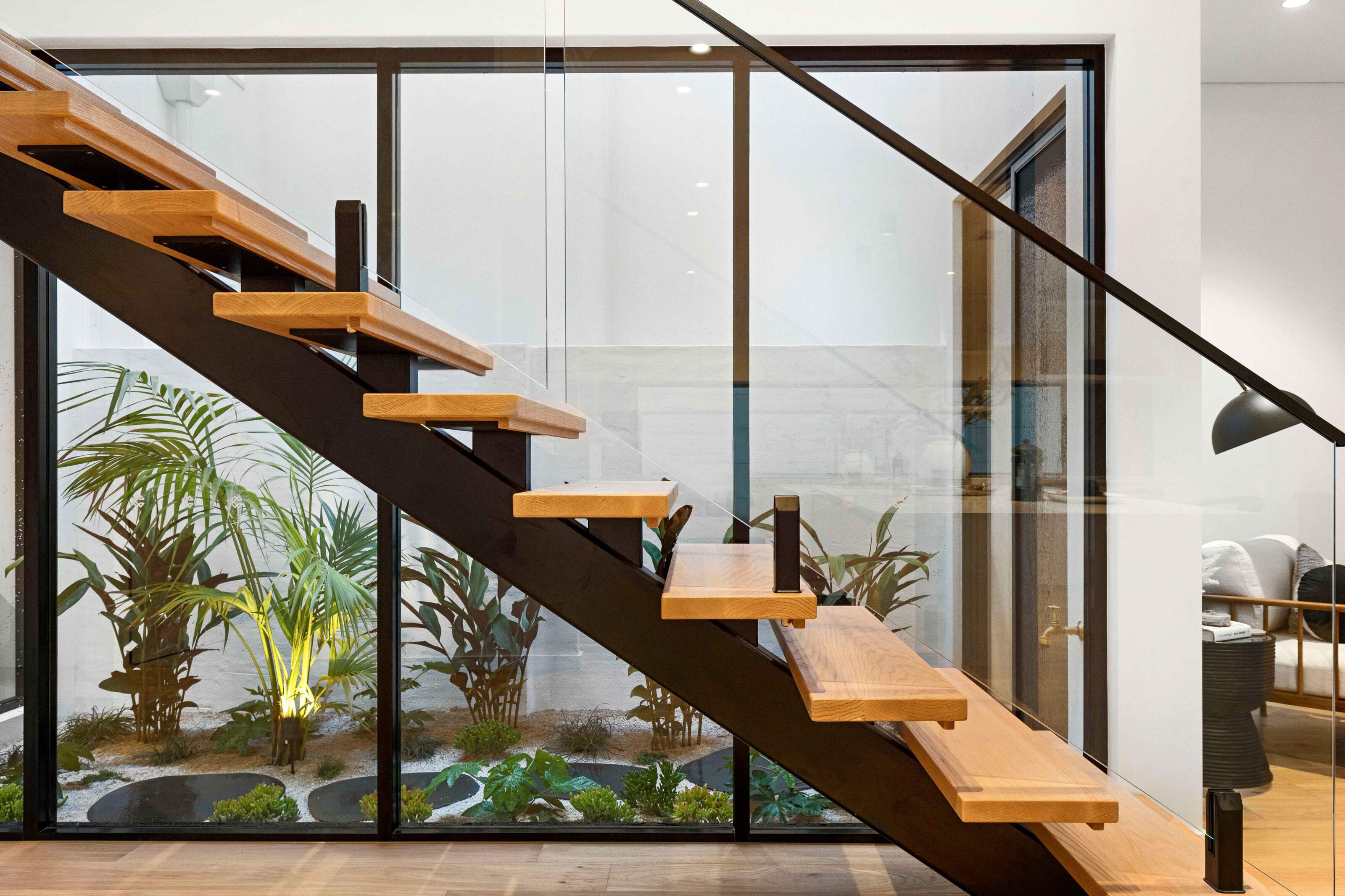 Timber open-riser staircase with glass balustrade beside an internal courtyard and large feature windows.