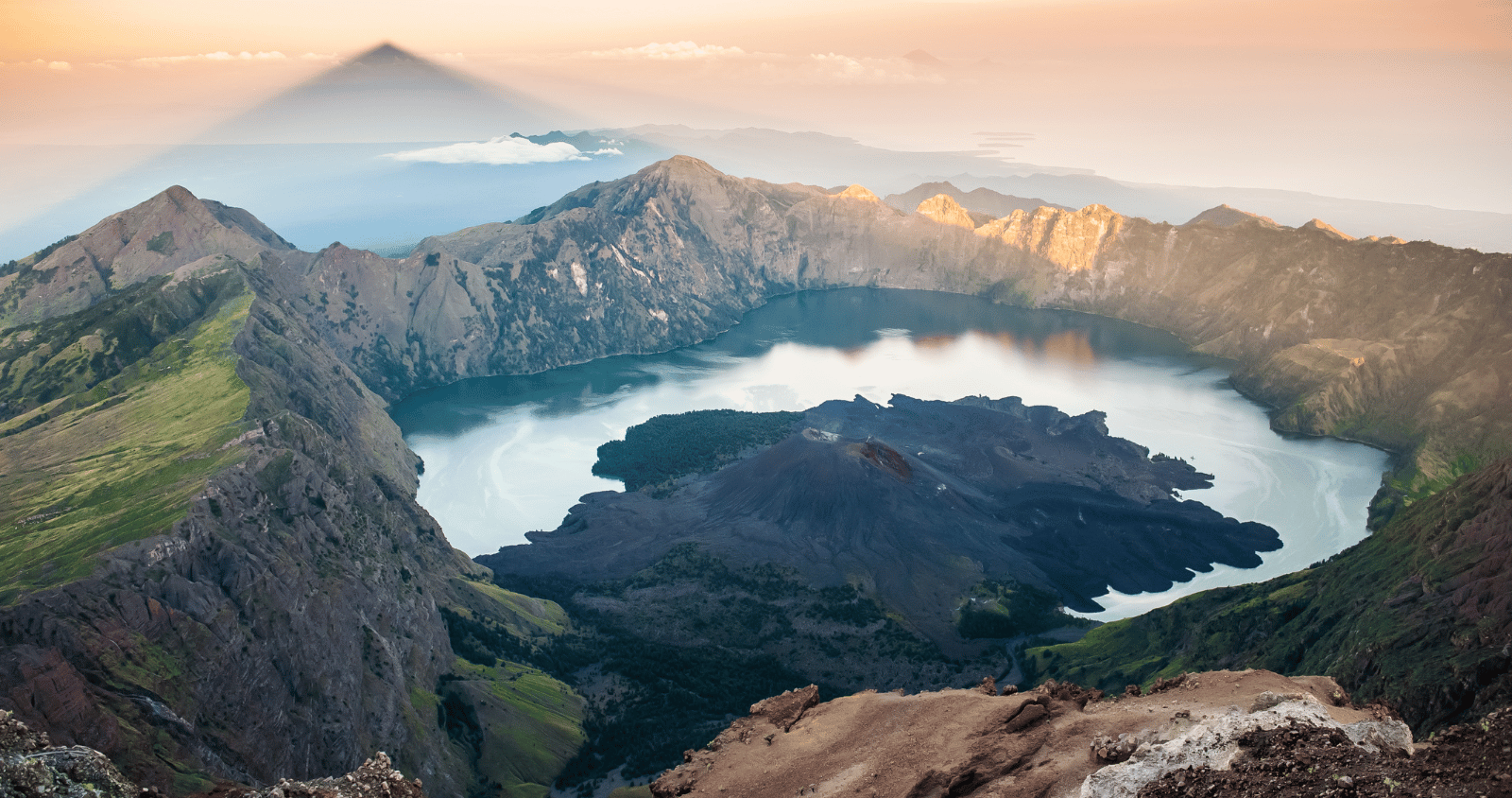 A panoramic view of Mount Rinjani’s crater lake Segara Anak under a clear blue sky, Lombok, Indonesia.
