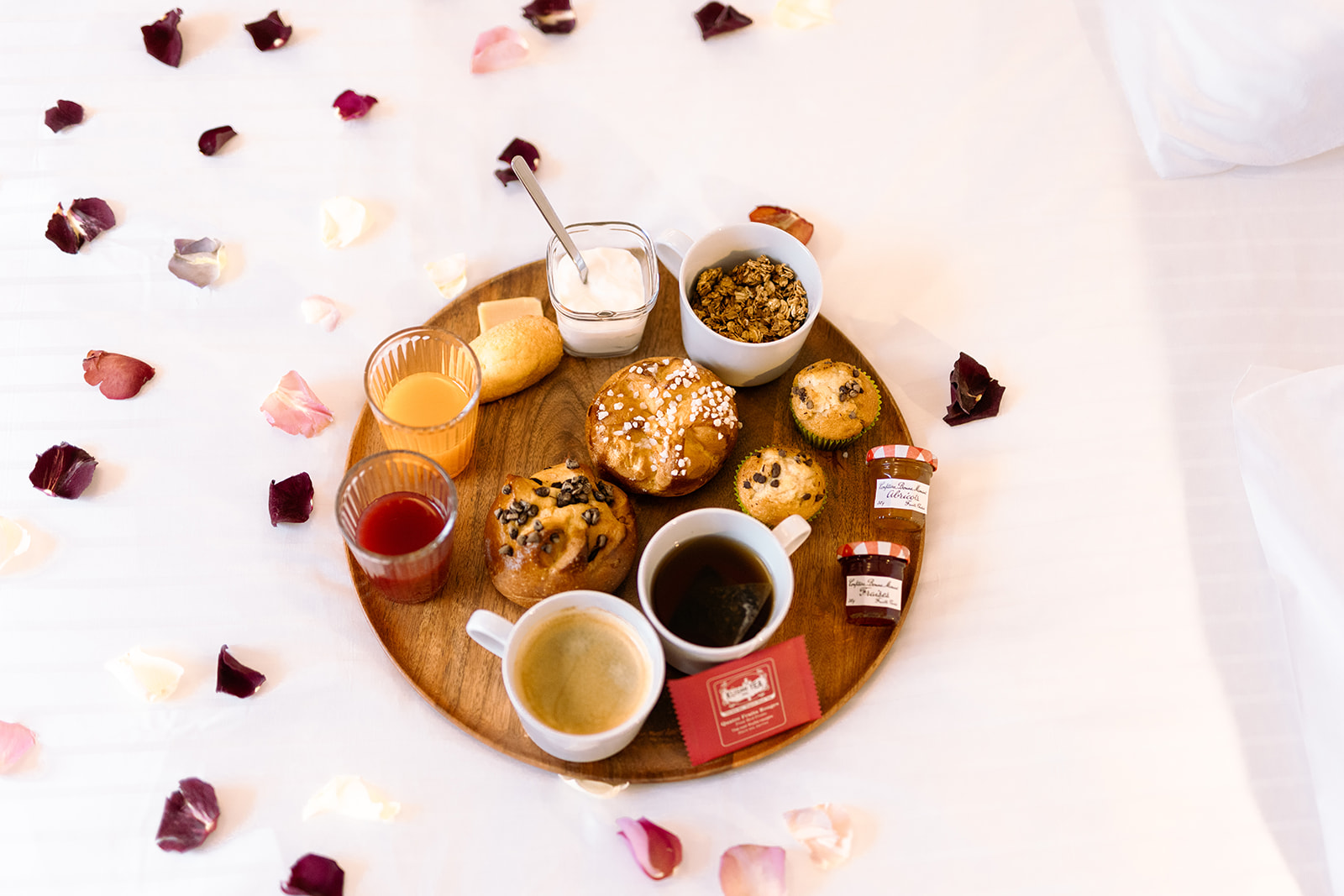 Petit déjeuner avec café, thé, jus, muffins, yaourt, confitures et pain sur plateau en bois.
