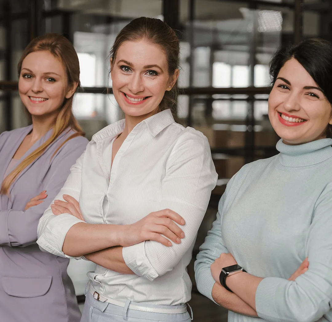 Tri nasmejane žene sa prekriženim rukama stoje u kancelariji.