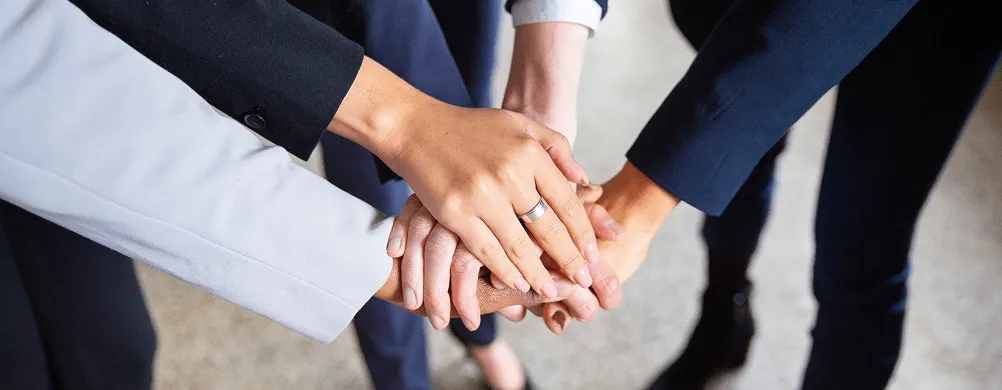 Više ruku različitih osoba složenih jednu preko druge kao simbol timskog rada i saradnje.