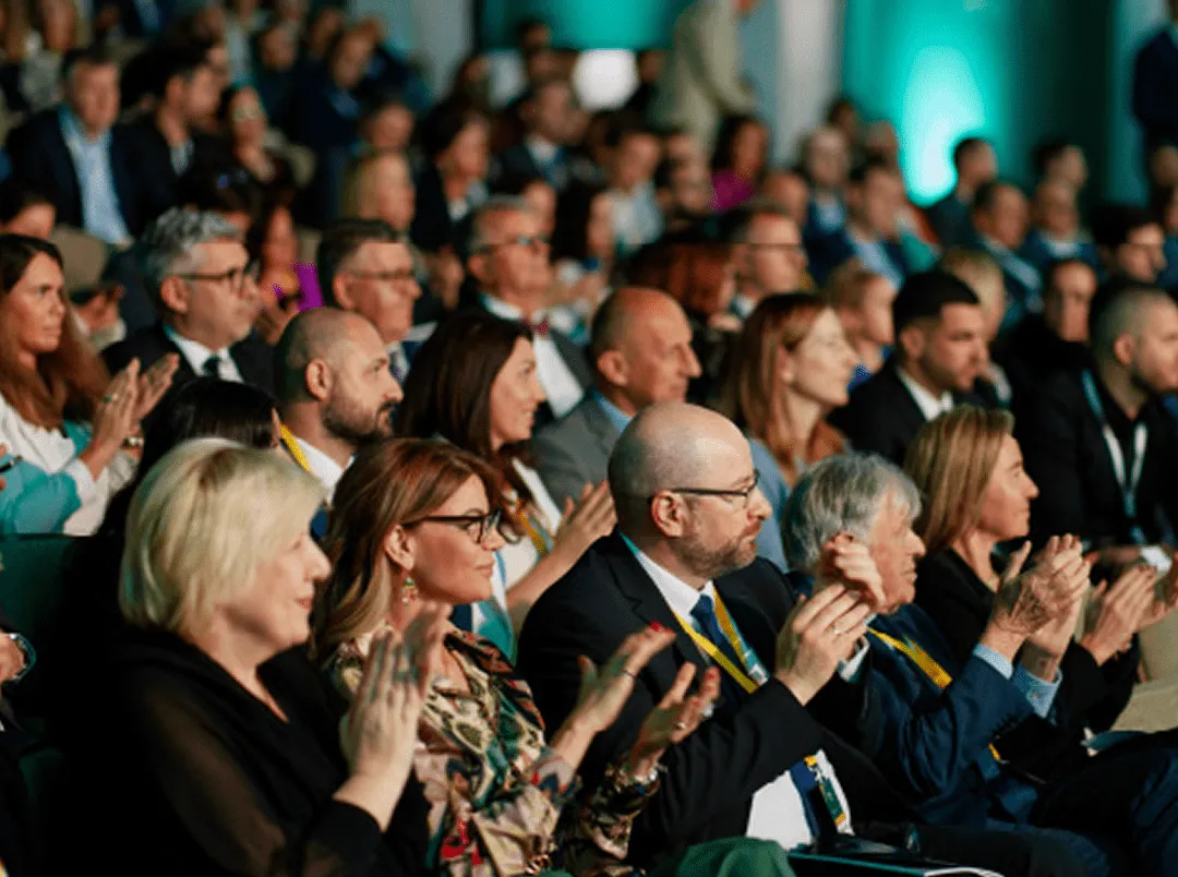 Skup ljudi sedi i aplaudira na konferenciji ili događaju.