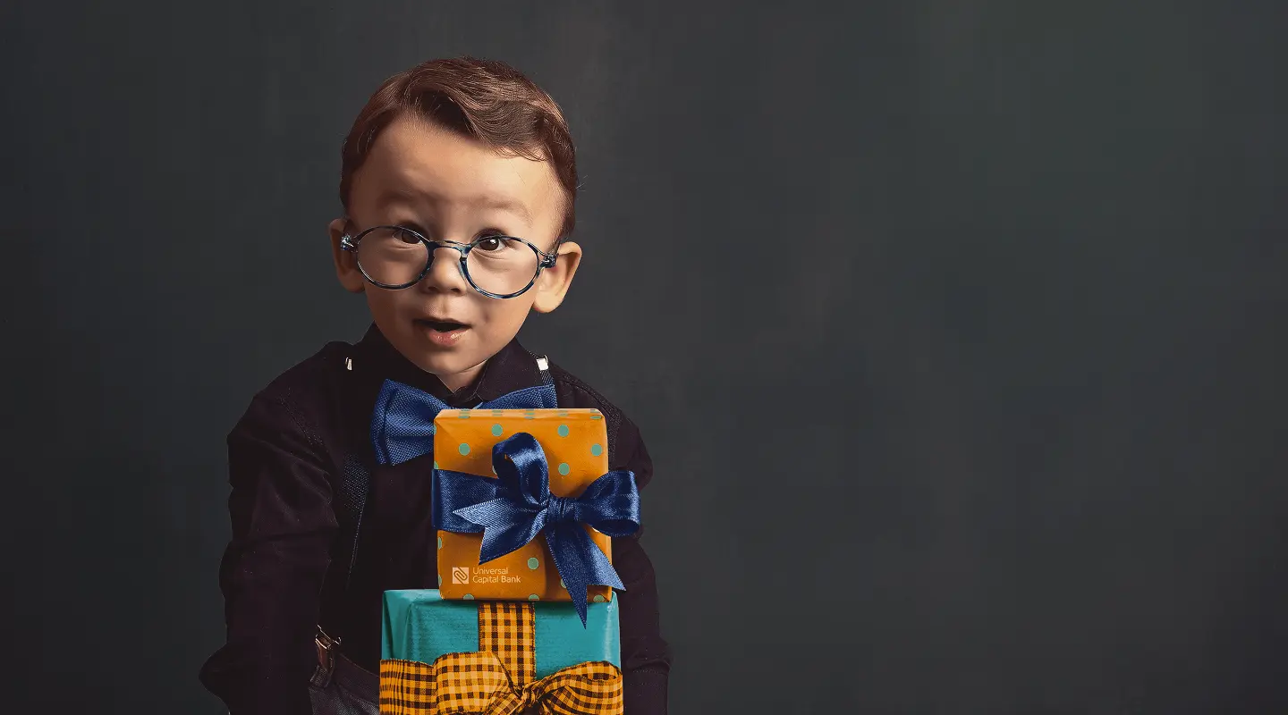 Mali dečak sa naočarima i plavom leptir-mašnom drži dva umotana poklona sa mašnama.