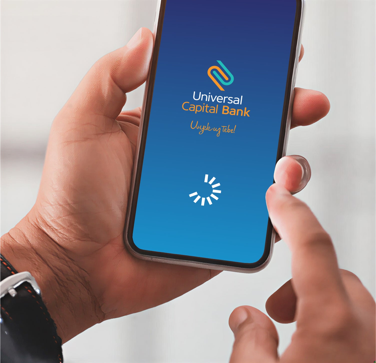 Ruka drži telefon sa ekranom Universal Capital Bank aplikacije koji se učitava.