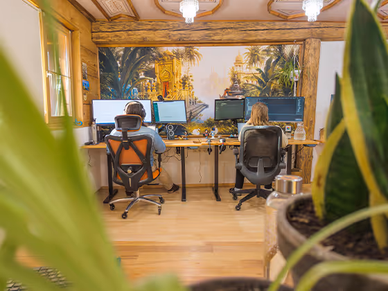 Mitarbeiter:innen von Leto AI arbeiten im offenen Büro mit Holzdekor und Dschungel-Wandmotiv an mehreren Monitoren