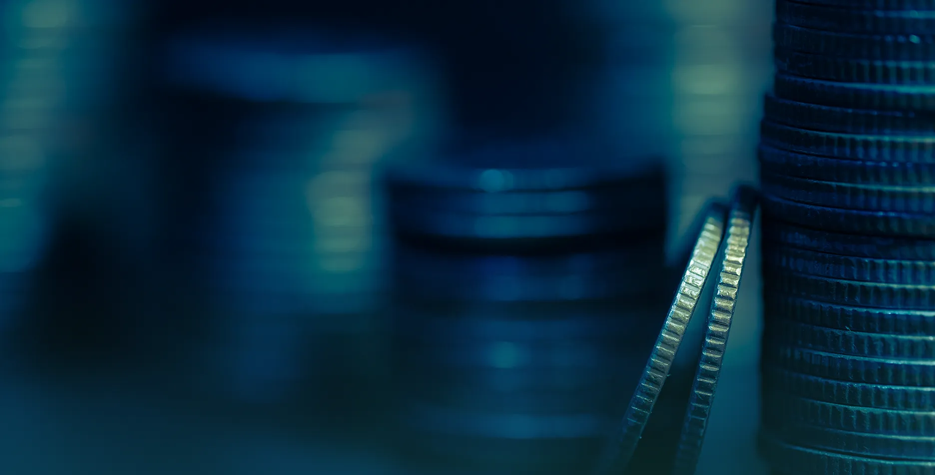 Close-up of stacks of coins with a blue tint, focusing on the ridged edges of two leaning coins.