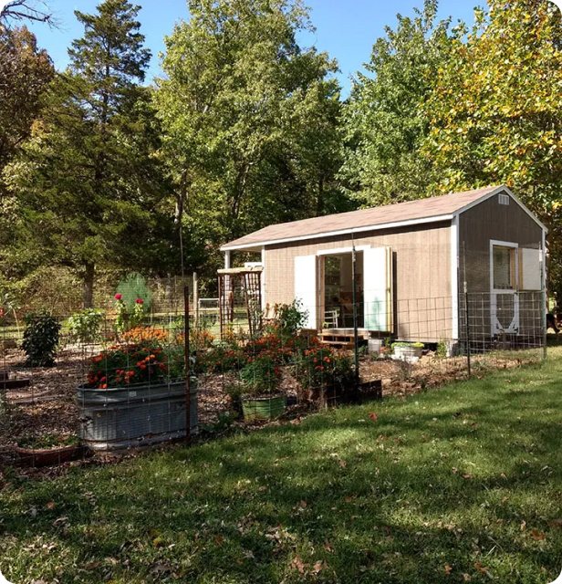Large wood A-frame she shed with deep porch beside garden