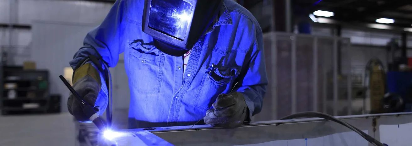Welder in protective gear working with bright blue welding arc