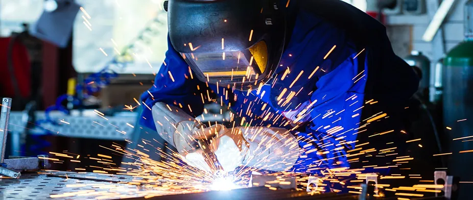 Welder in blue protective gear working with bright sparks flying