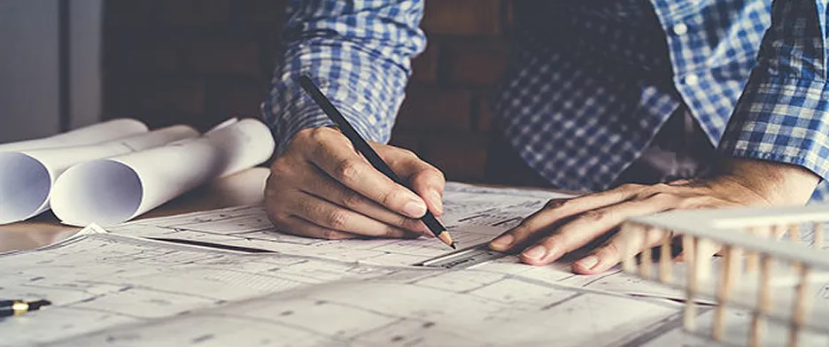 Architect working on blueprints with pencil at drafting table