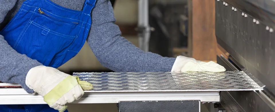 Worker in blue overalls handling metal grate with protective gloves