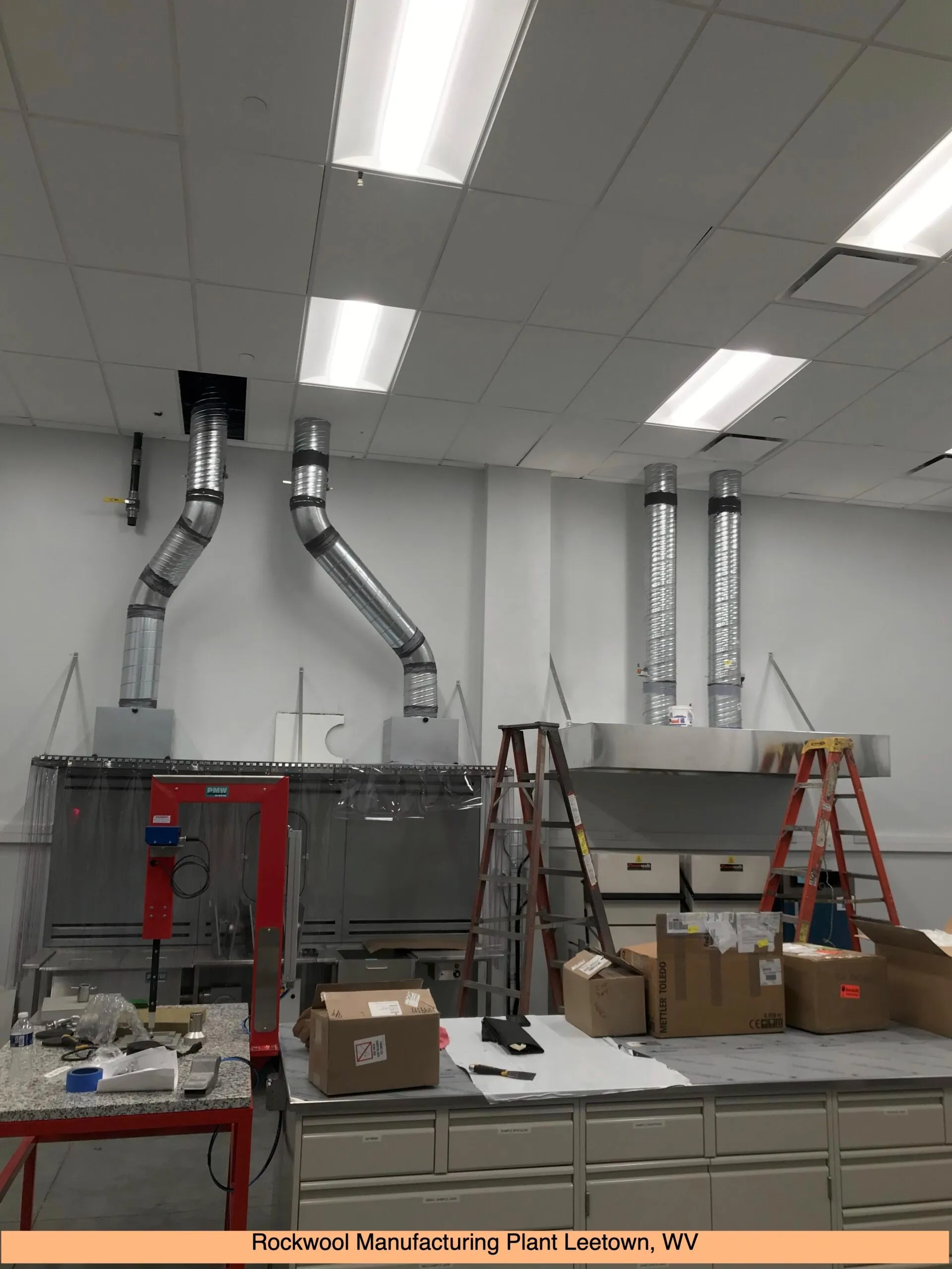 Industrial workspace with ventilation ducts, machinery, ladders, and cardboard boxes