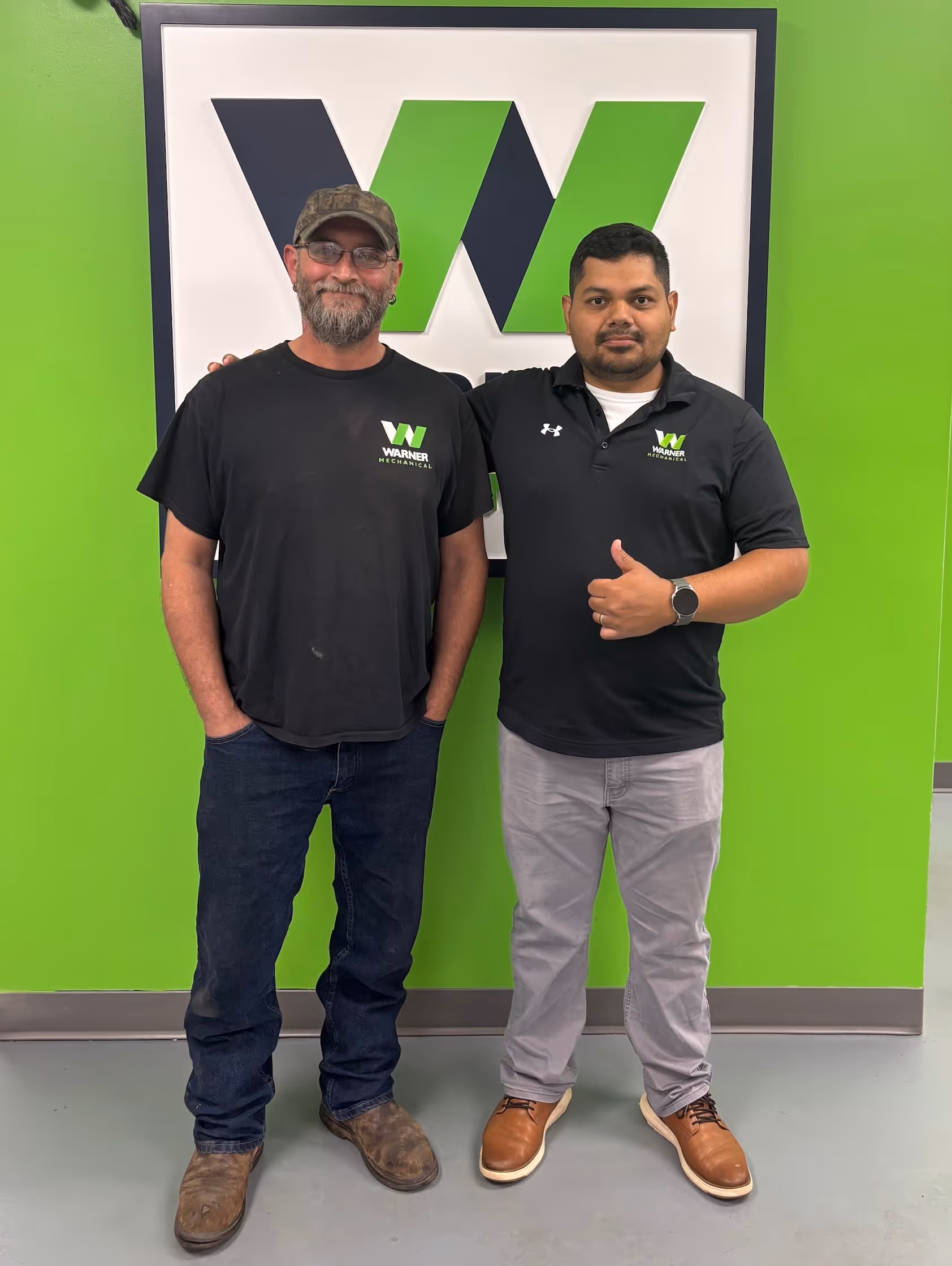 Two Warner Mechanical employees posing in front of company logo