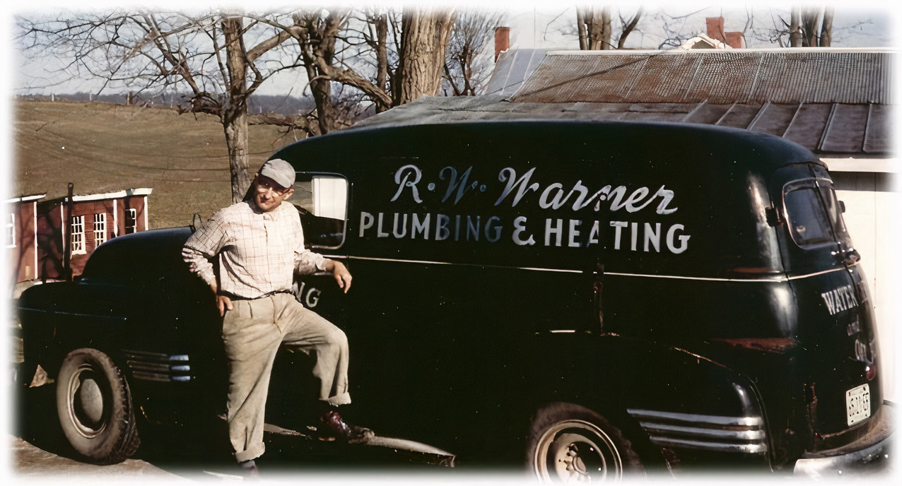 A man poses next to an R.W. Warner plumbing and heating truck with a rural landscape in the background.