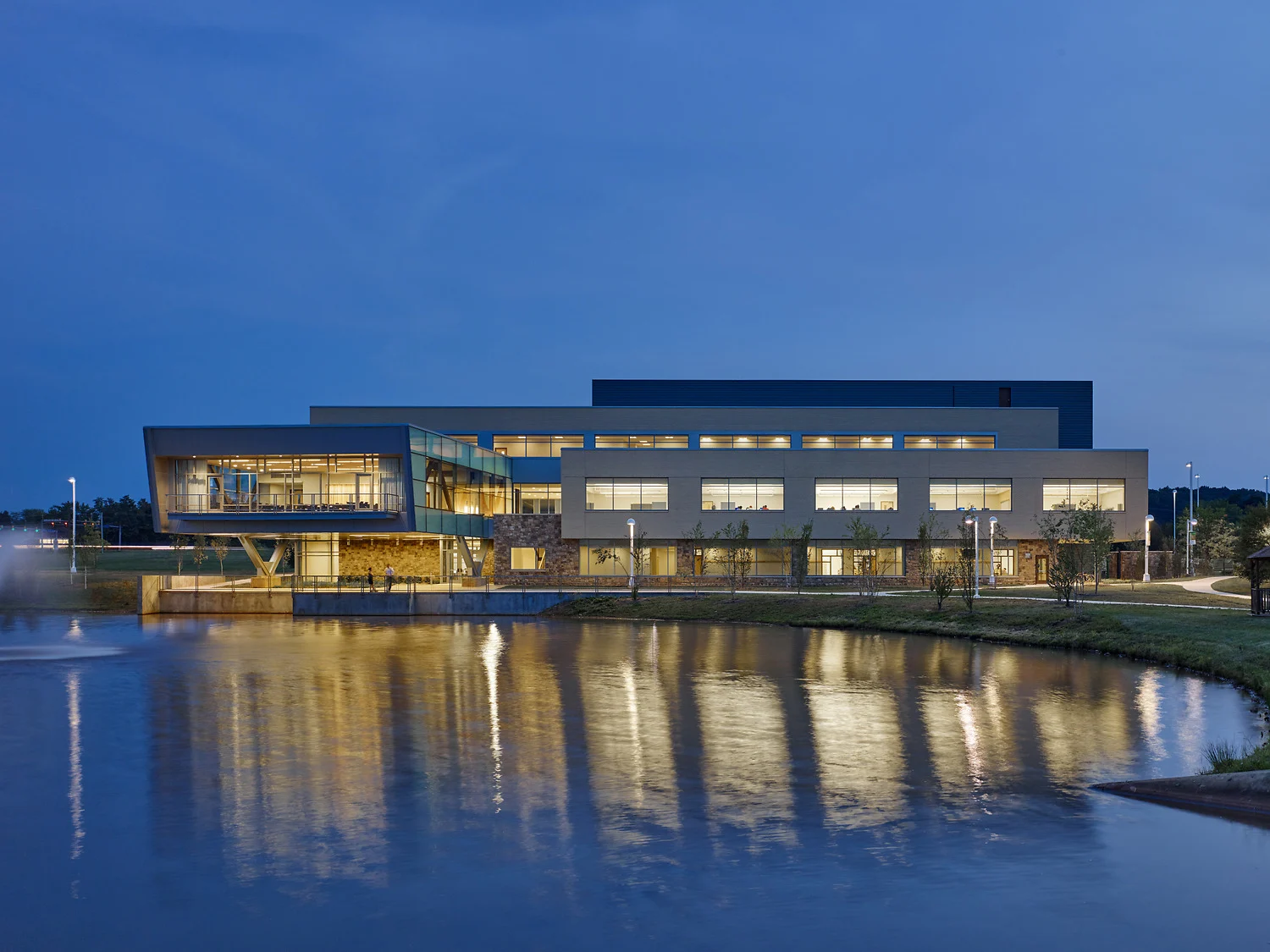 A modern building at dusk, reflected in a pond.