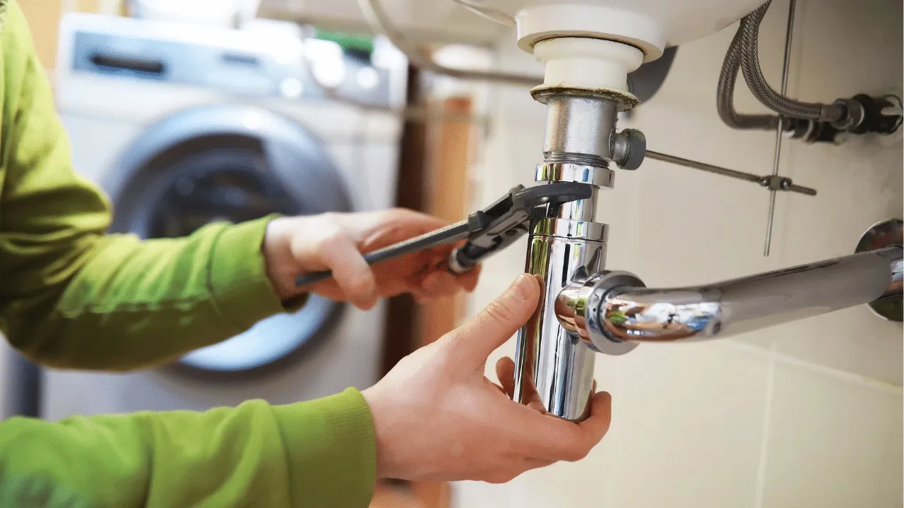 Person with wrench fixes sink plumbing.