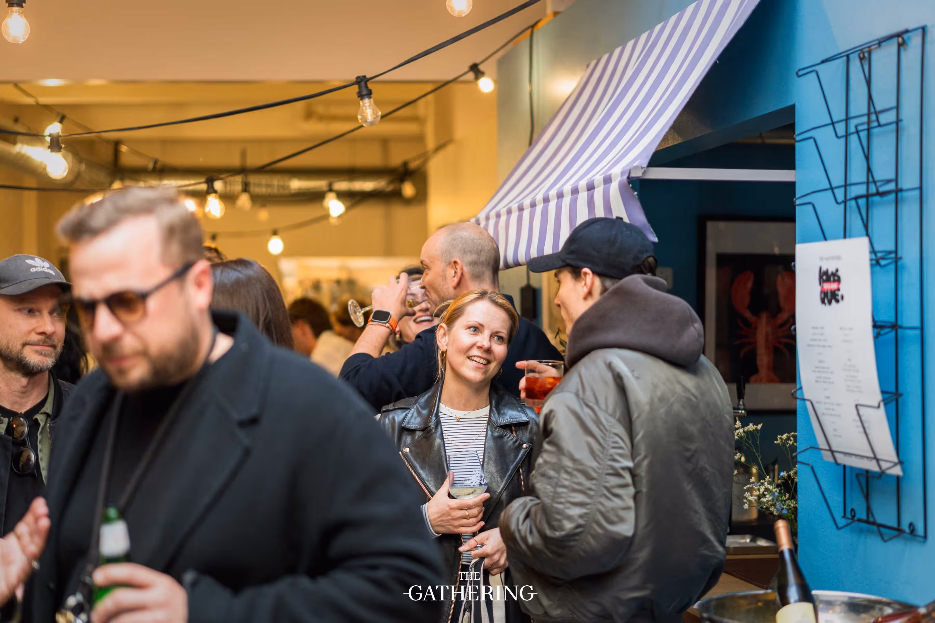 Crowd mingling around tables with drinks at The Gathering hosted by Maison ACME