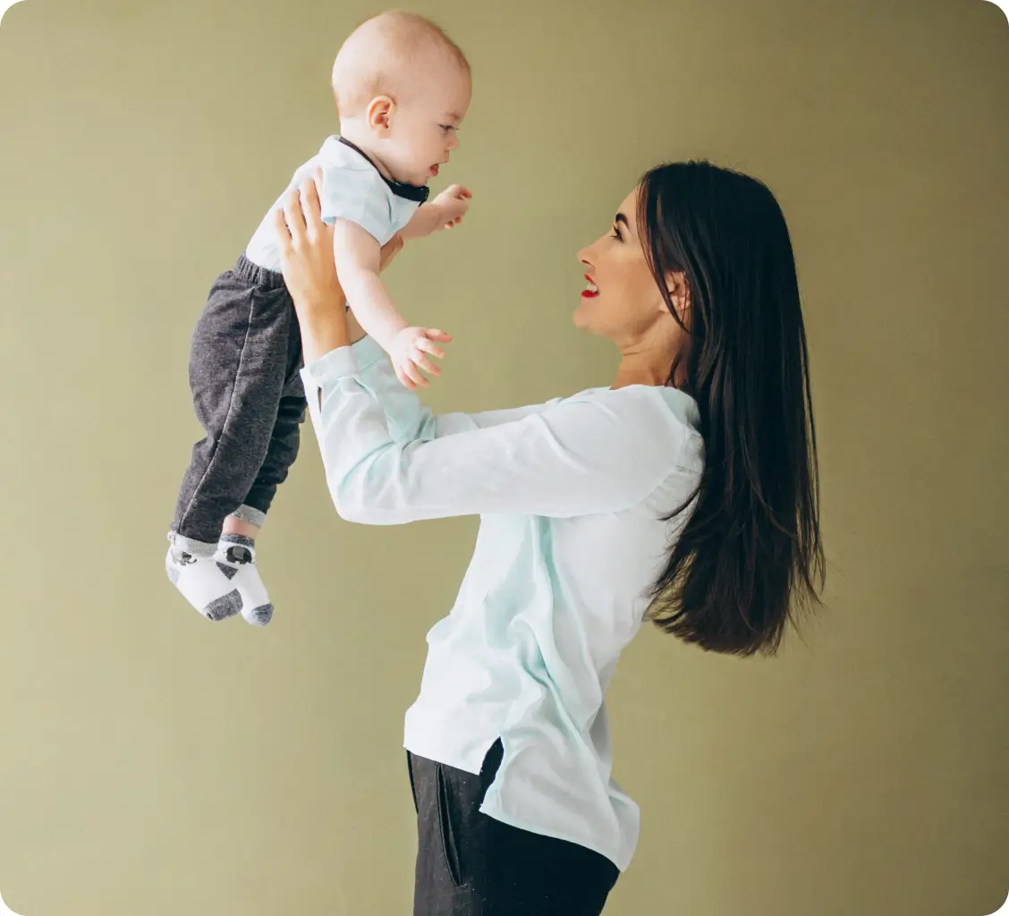 Young woman holding a baby in her arms and smiling while lifting the baby into the air