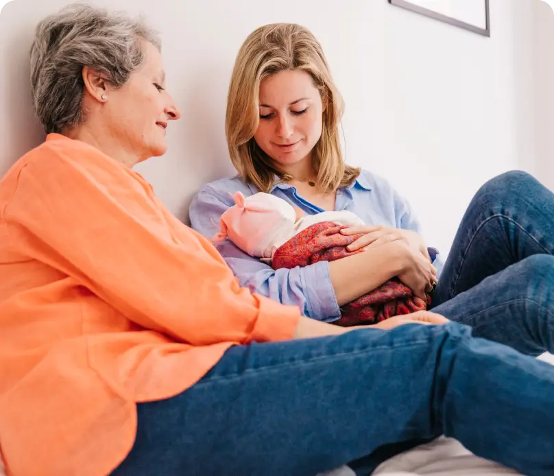 Mother holding a newborn baby with a healthcare professional nearby