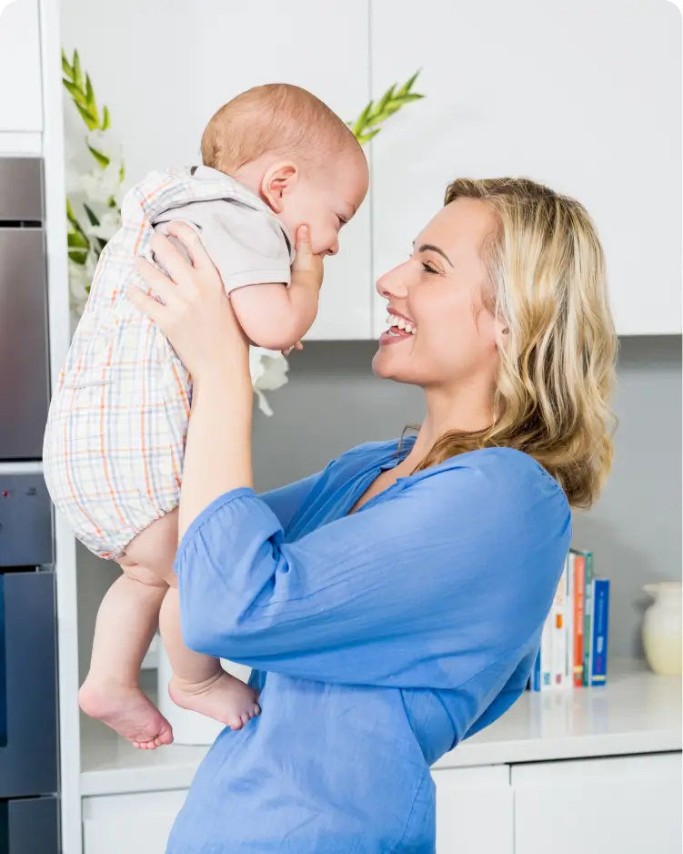 A nurse is smiling while holding a small baby in her arms and lifting them up