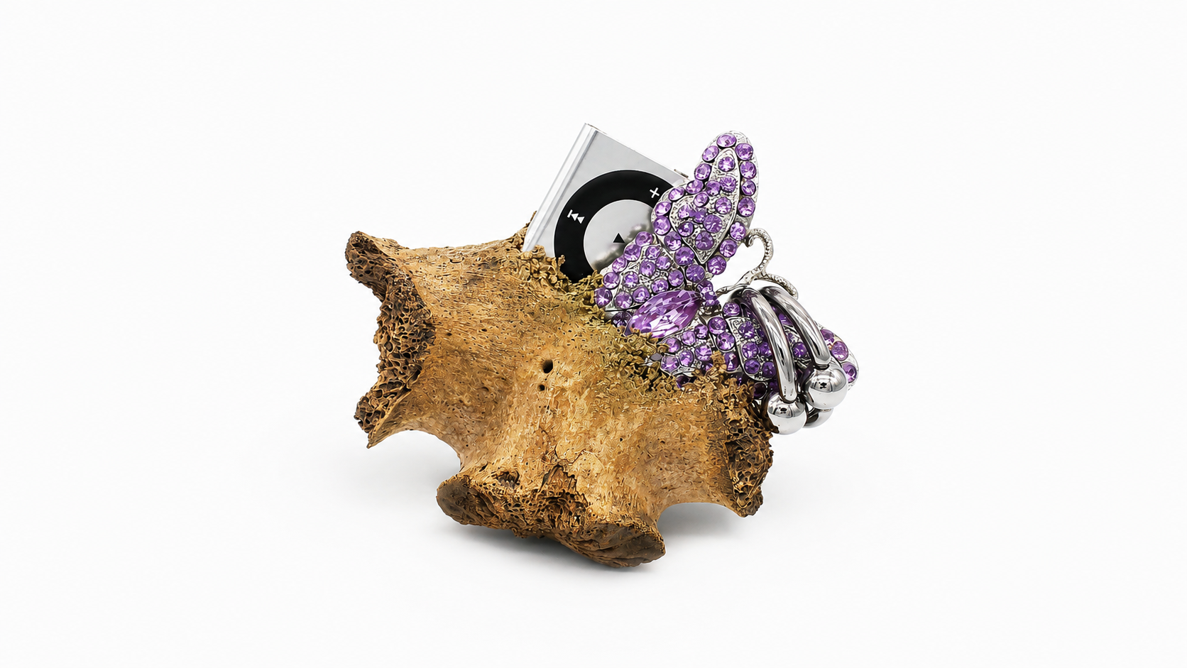 Skulptur ’Not Compatible’ von Corrina Goutos aus einem organisch wirkenden Fundstück, einem MP3-Player und violettem Schmuck auf weißem Hintergrund.