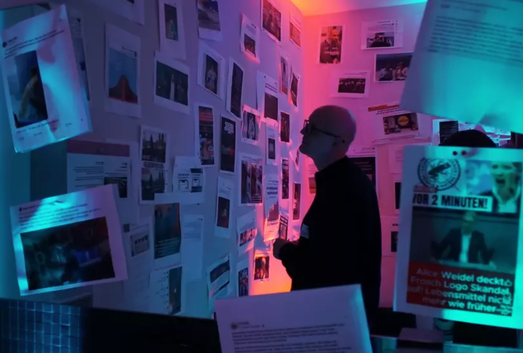 Ein Mann steht vor einer Bilder- und Nachrichtenwand im Dunklen