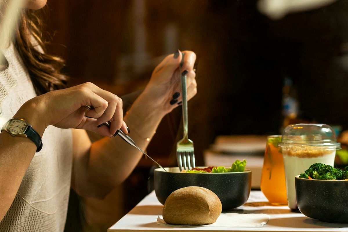 Frau isst Salat aus einer kleinen Schüssel, auf dem Tisch liegt ein Stück Brot und ein Saft.