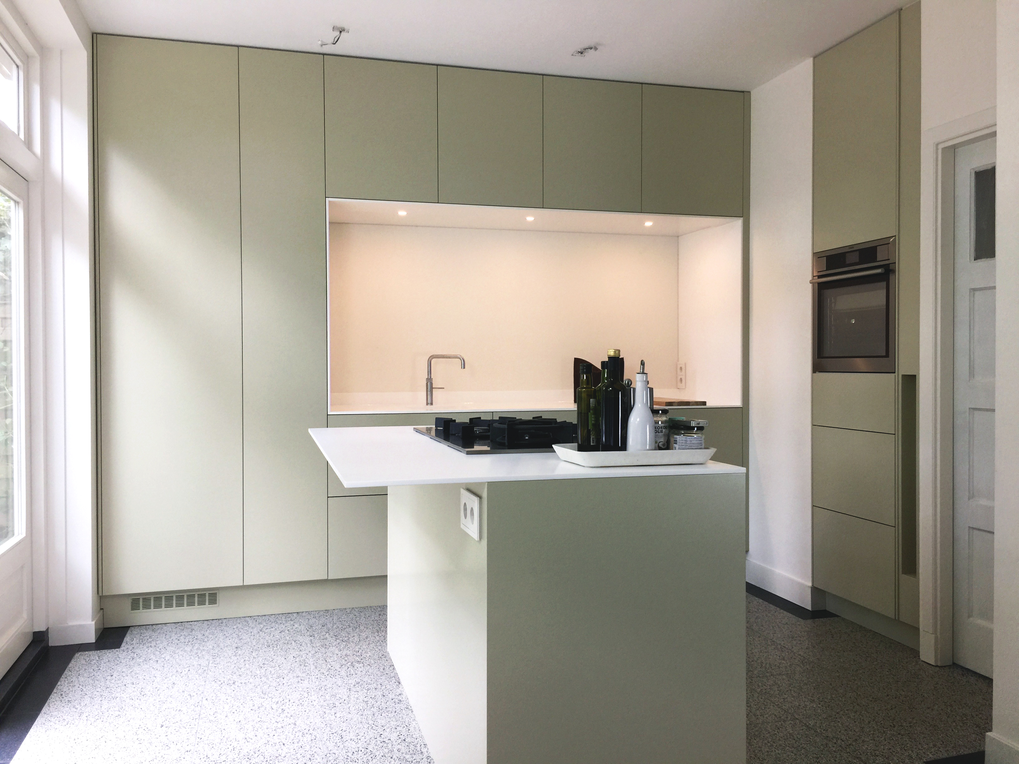 Moderne groene keuken met kookeiland en ingebouwde oven naast een witte deur.
