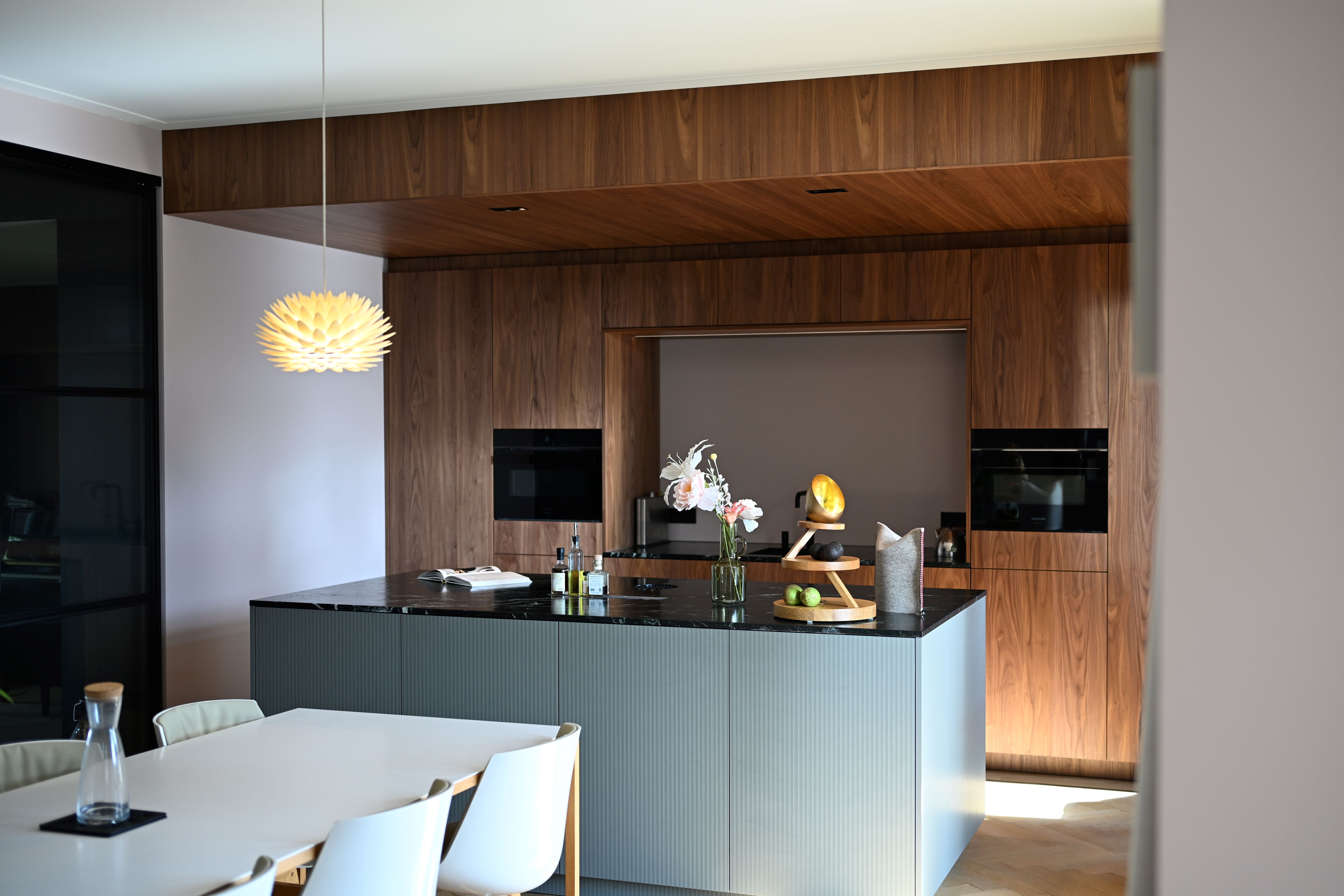 Moderne keuken met zwart granieten kookeiland, houten kasten en witte eettafel met stoelen.