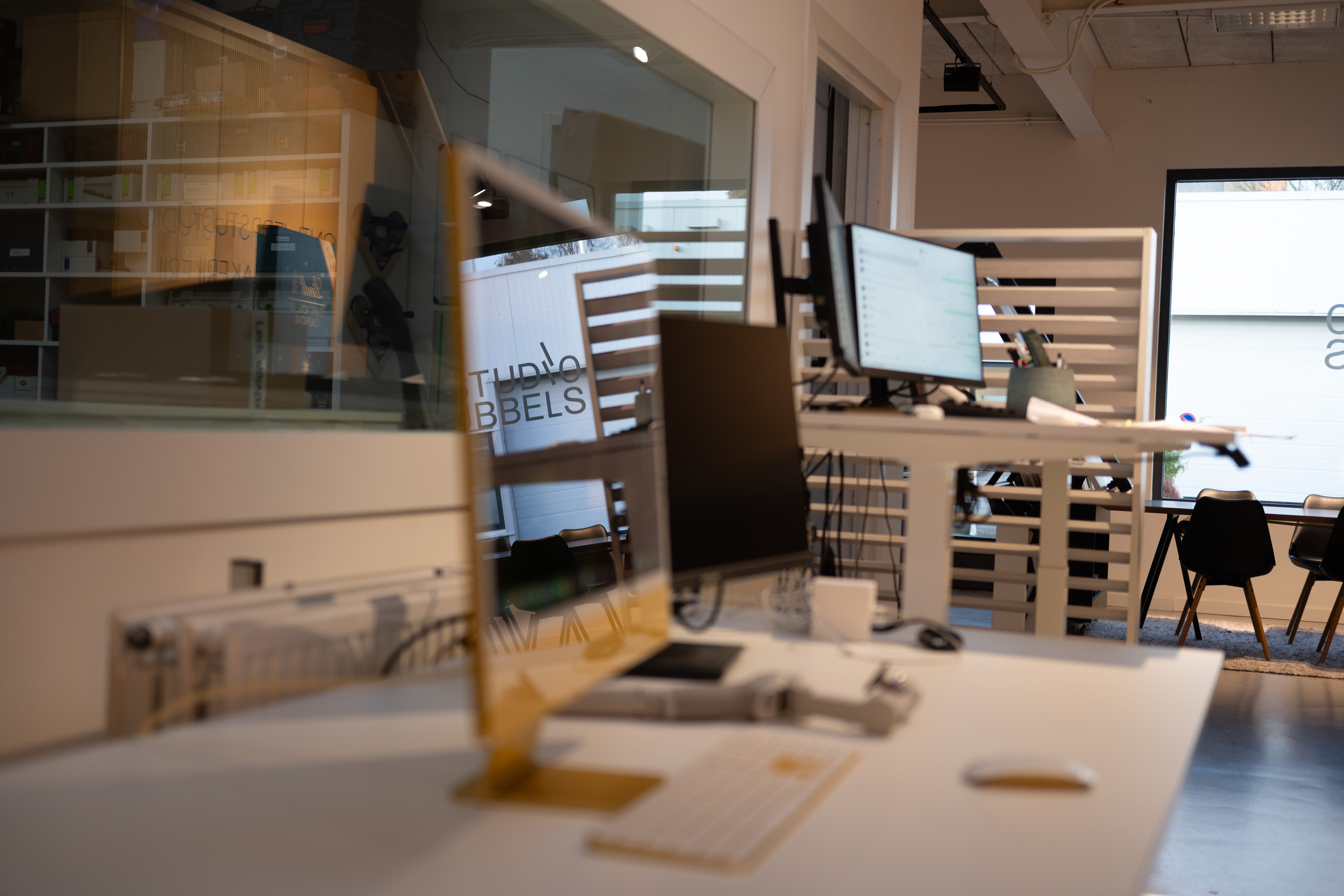 Modern office with desks, computers, chairs, and a reflection of 'STUDIO BUBBELS' on glass.
