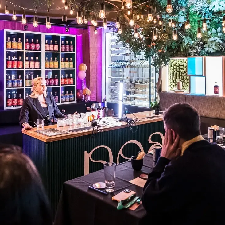 A female bartender is presenting her drink to an attentive judge at the Beyond NOA competition.
