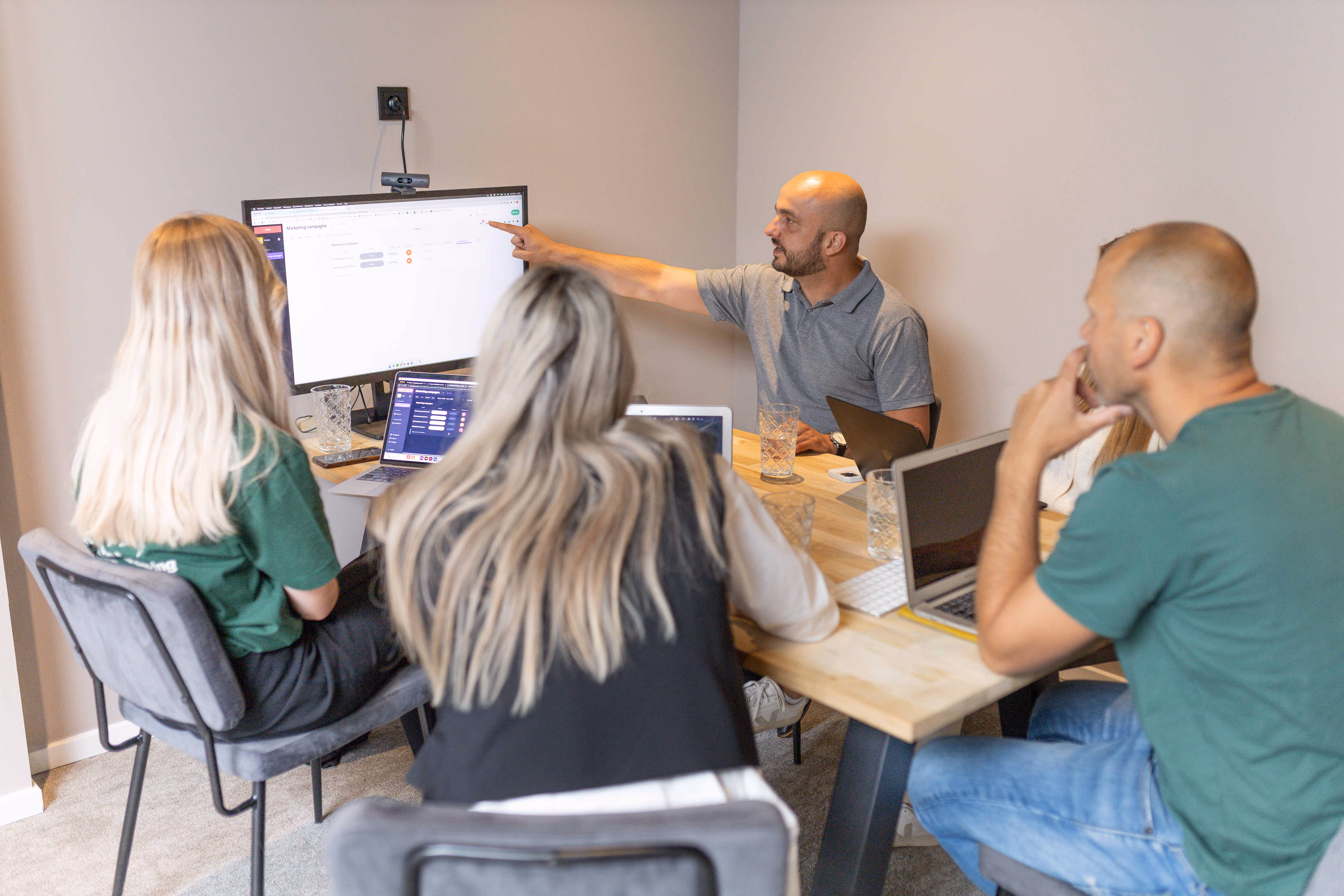 Teamleden van vPlan in overleg in een vergaderruimte, waarbij een collega een schermpresentatie geeft met uitleg over de planningsoftware.