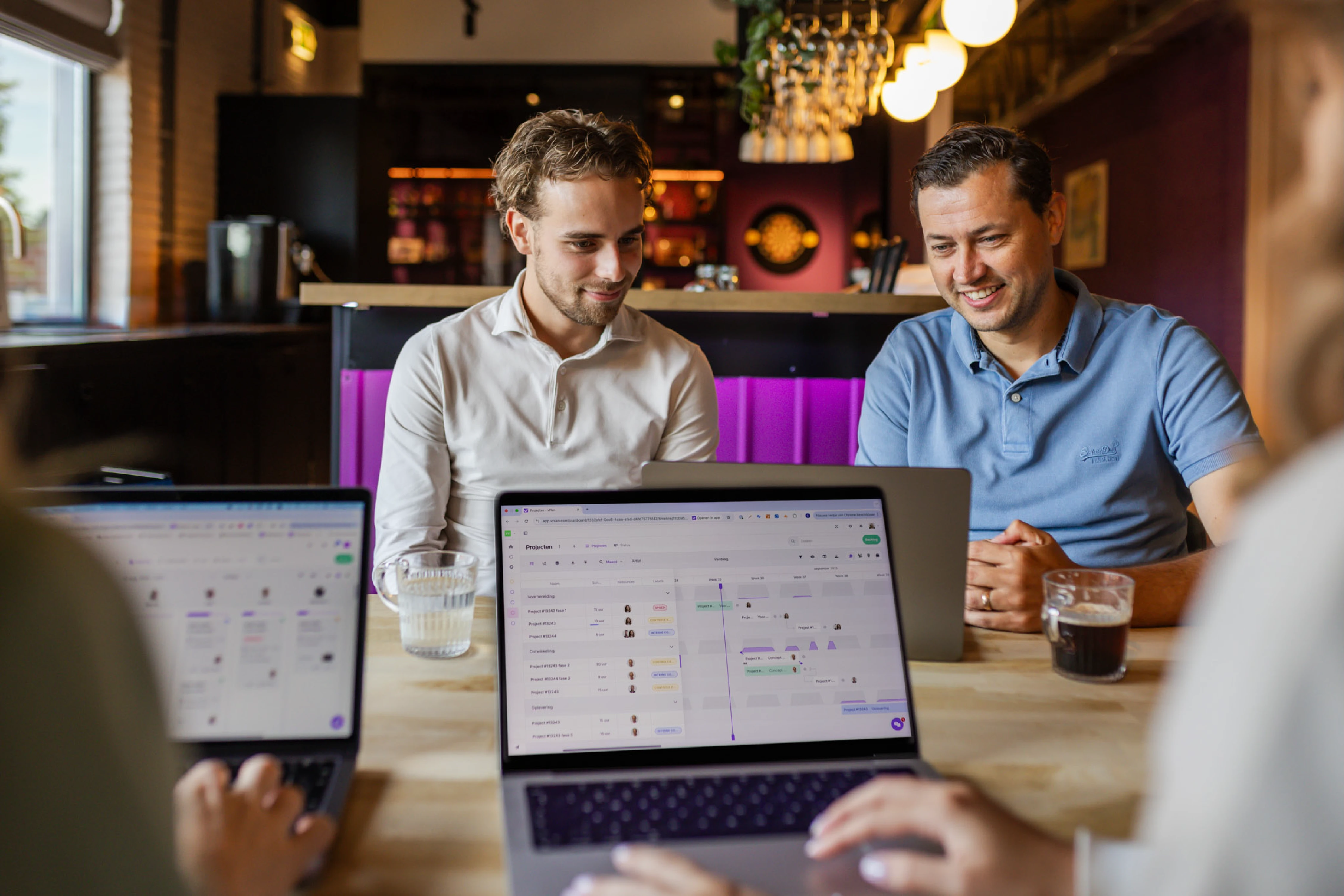 vPlan-team overlegt over capaciteitsplanning op kantoor, met de planningstool van vPlan zichtbaar op hun laptops.