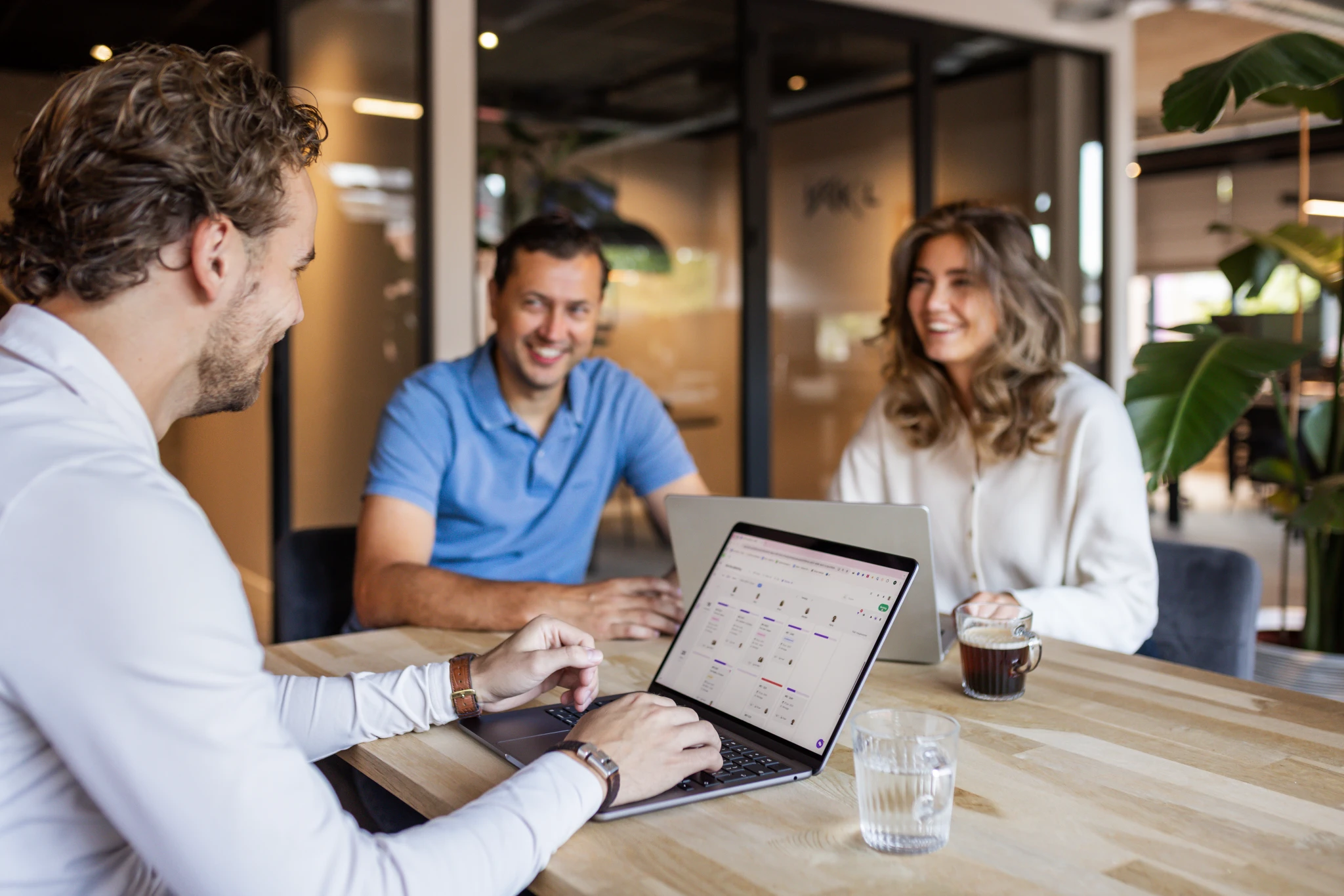 Team bespreekt projectplanning met vPlan op laptops tijdens een vergadering, in een moderne kantooromgeving met focus op samenwerking en efficiëntie.