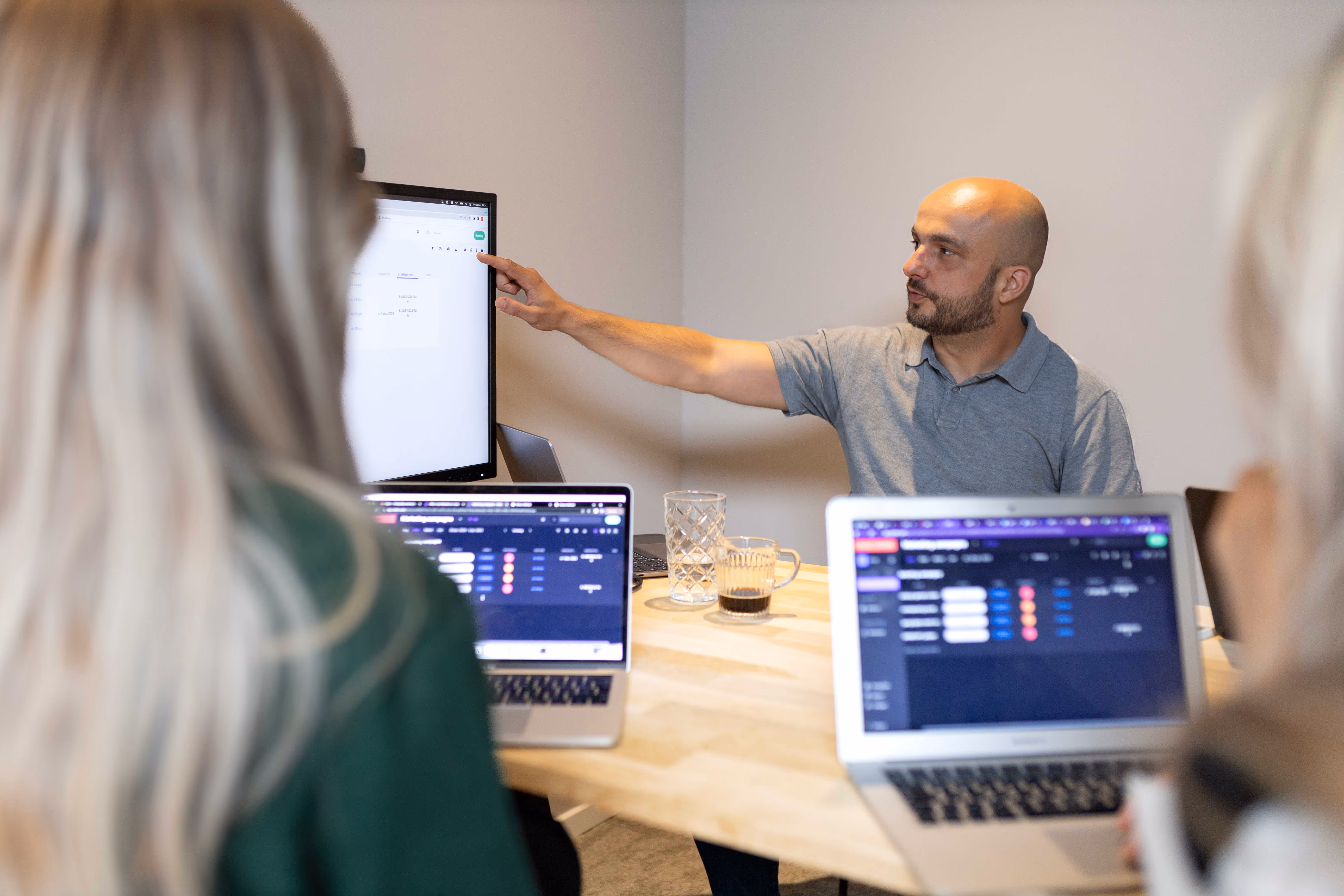 Team meeting where a team member presents a planning on a screen while colleagues collaborate with laptops around the table.
