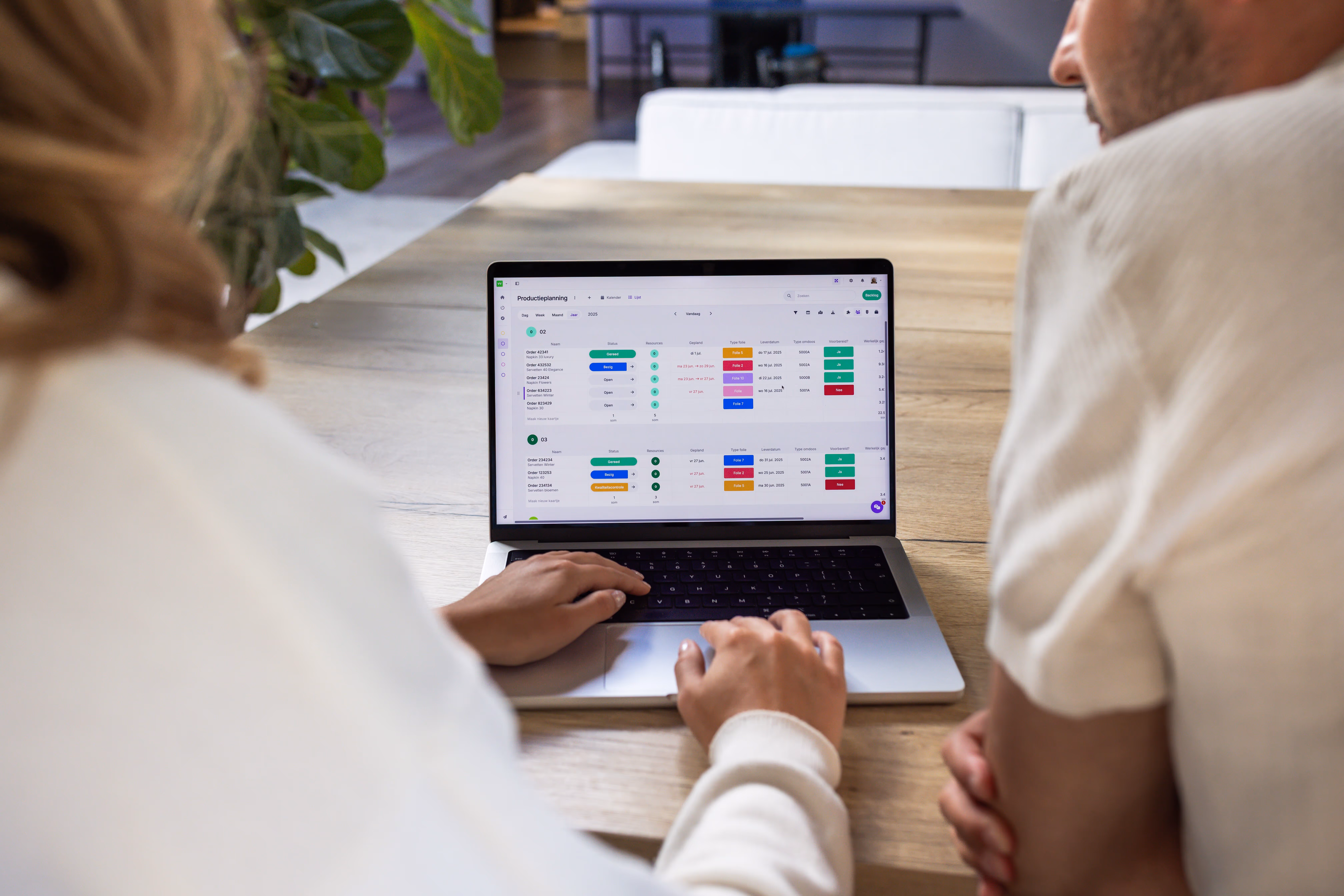 Team meeting discussing project planning using vPlan, with a colleague pointing at a screen and laptops showing the planning tool.