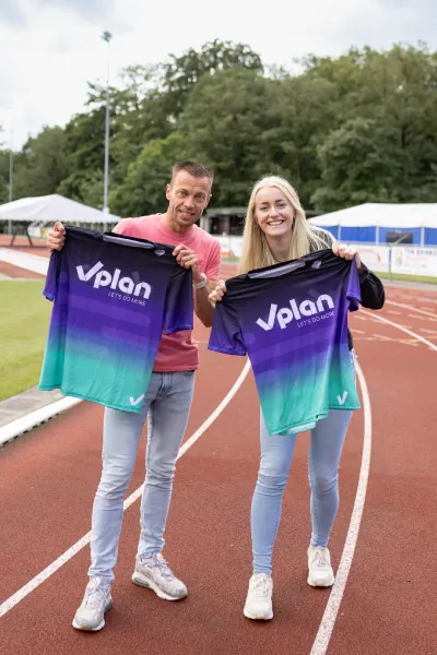 Man and woman on a running track holding purple and teal gradient Vplan sports shirts.