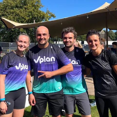 Group of four adults in athletic wear posing outdoors under a tent on a sunny day.