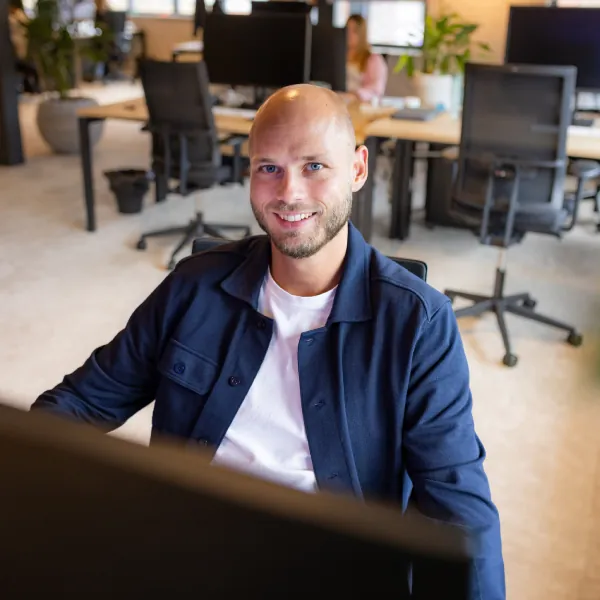 Smiling bald man with beard sitting at a desk in a modern office environment.