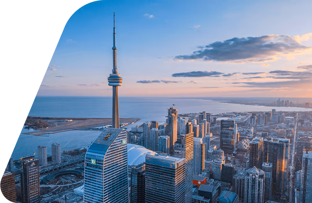 Toronto skyline at sunset with CN Tower overlooking buildings and Lake Ontario in the background.