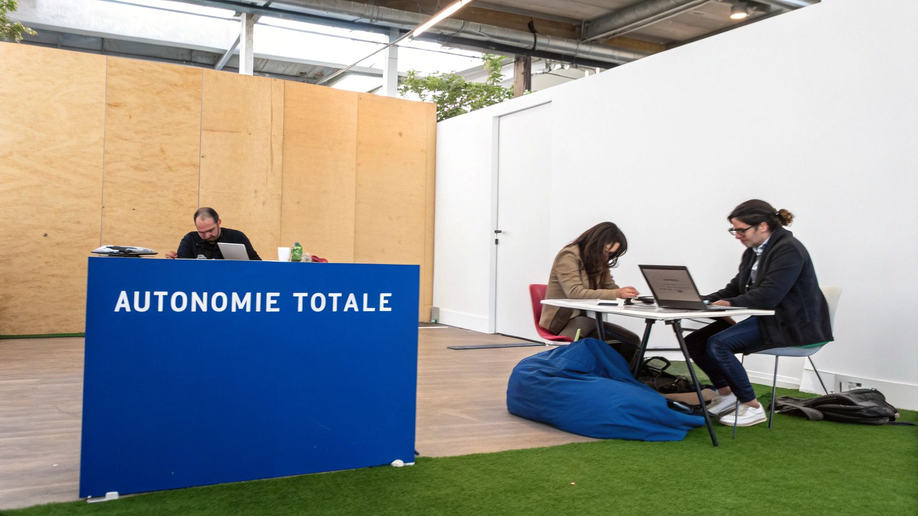 Trois personnes travaillant sur des ordinateurs portables dans un espace de bureau moderne avec un signe «AUTONOMIE TOTALE».