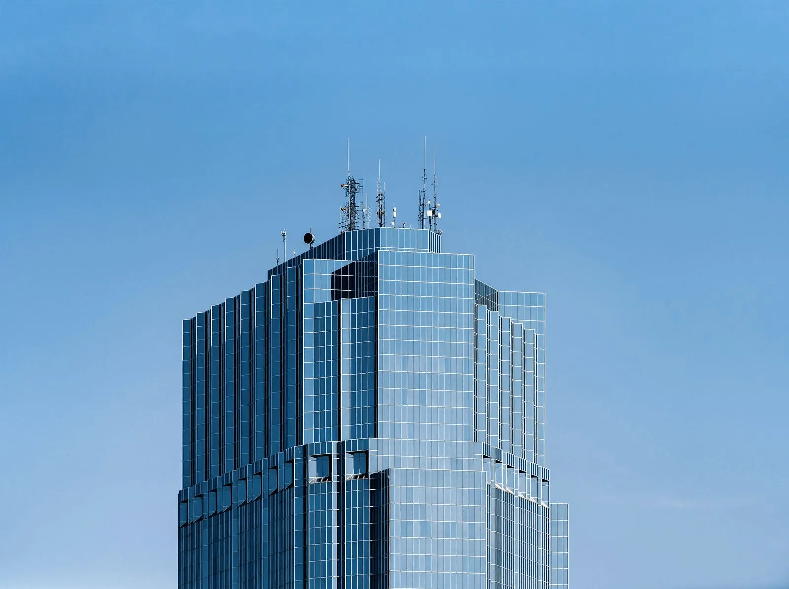 Modern glass building with antennas and structures on the rooftop under a clear blue sky