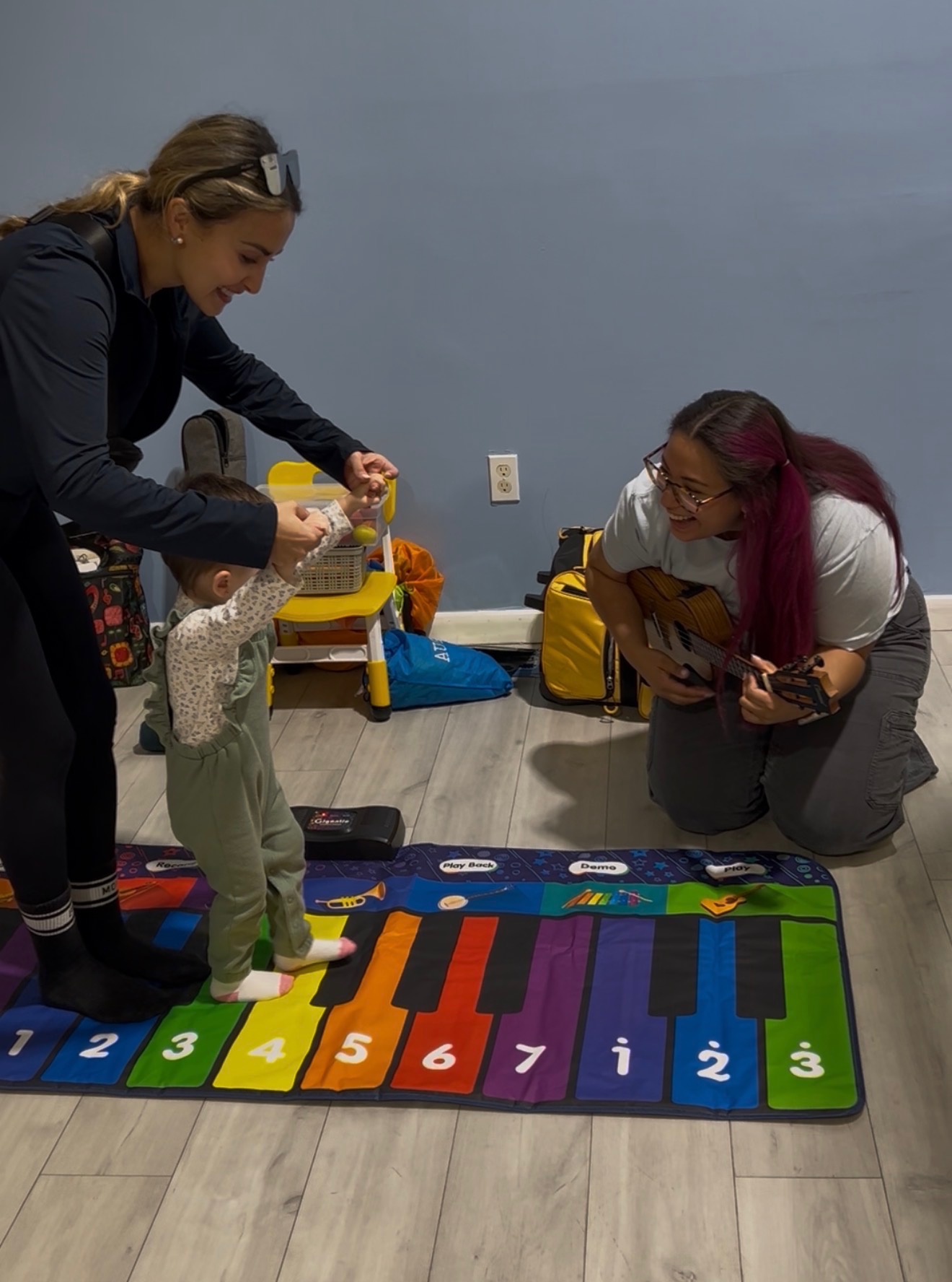 Gabriela and a caregiver helping a toddler move to live ukulele music