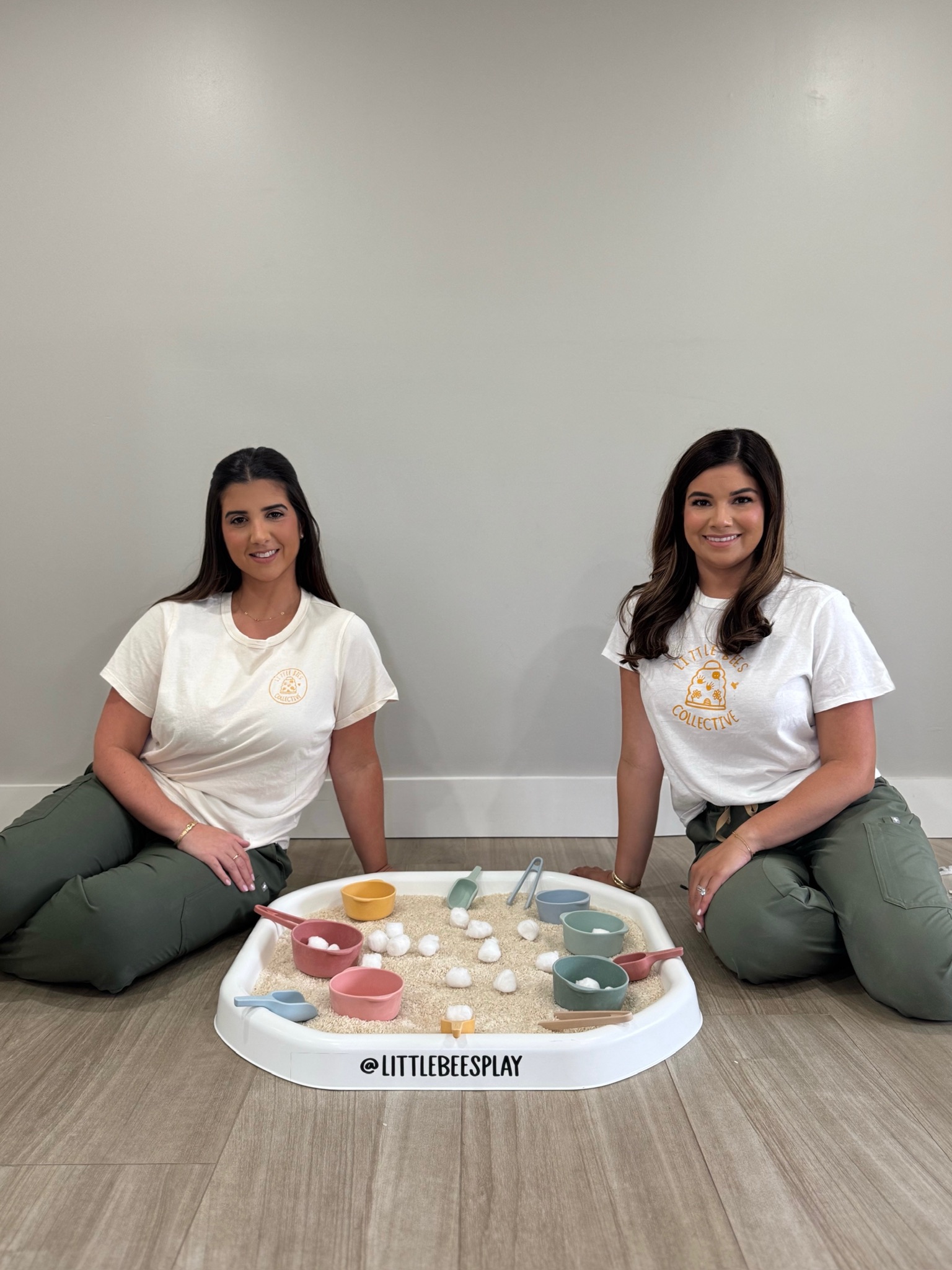 Two Little Bees providers sit beside a prepared sensory play bin.